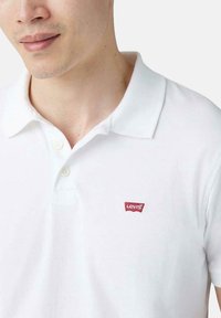 Camisa polo blanca de algodón, con cuello clásico, tres botones y un pequeño logo rojo de Levi's en el lado izquierdo del pecho.