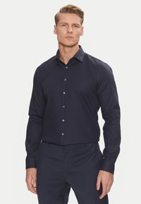 Maglietta a maniche lunghe blu navy con un motivo testurizzato, chiusura con bottoni e colletto strutturato. Presenta bottoni argentati e un design slim fit.