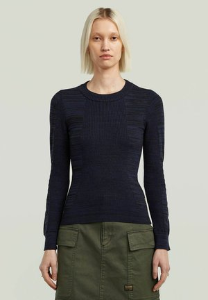 Pull en tricot navy avec une texture côtelée et des manches longues, présentant différents motifs et un col rond. Associé à une jupe verte.