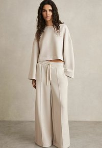 Felpa beige corta con maniche larghe abbinata a pantaloni a gamba larga con vita alta. Texture liscia, vita con cordoncino, design minimalista.