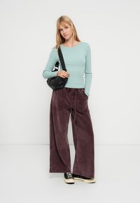 Haut bleu clair à manches longues côtelé, pantalon large bordeaux avec cordon de serrage ajustable, sac bandoulière noir et baskets noires.