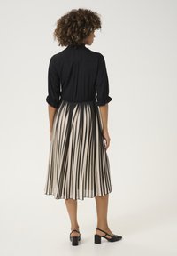 Čierny top s trojštvrťovými rukávmi, sťahovaný v páse, prúžkovaná suknia v béžovej a čiernej farbe, doplnená čiernymi sandálmi na vysokom opätku.