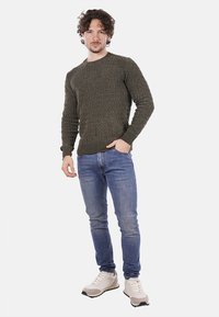Suéter verde de punto con un patrón texturizado, escote redondo; combinado con jeans azules y zapatillas de color claro.