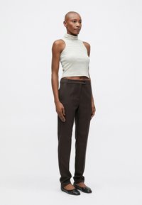Ujjatlan, világoszöld csíkos cropped top magas nyakkal; sötétbarna, szabott nadrággal és fekete lapos cipővel viselve.