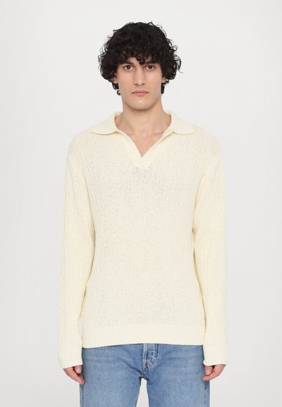 Light yellow knitted sweater with a v-neck and a soft collar. Features long sleeves and a textured pattern throughout. Worn with blue jeans.
