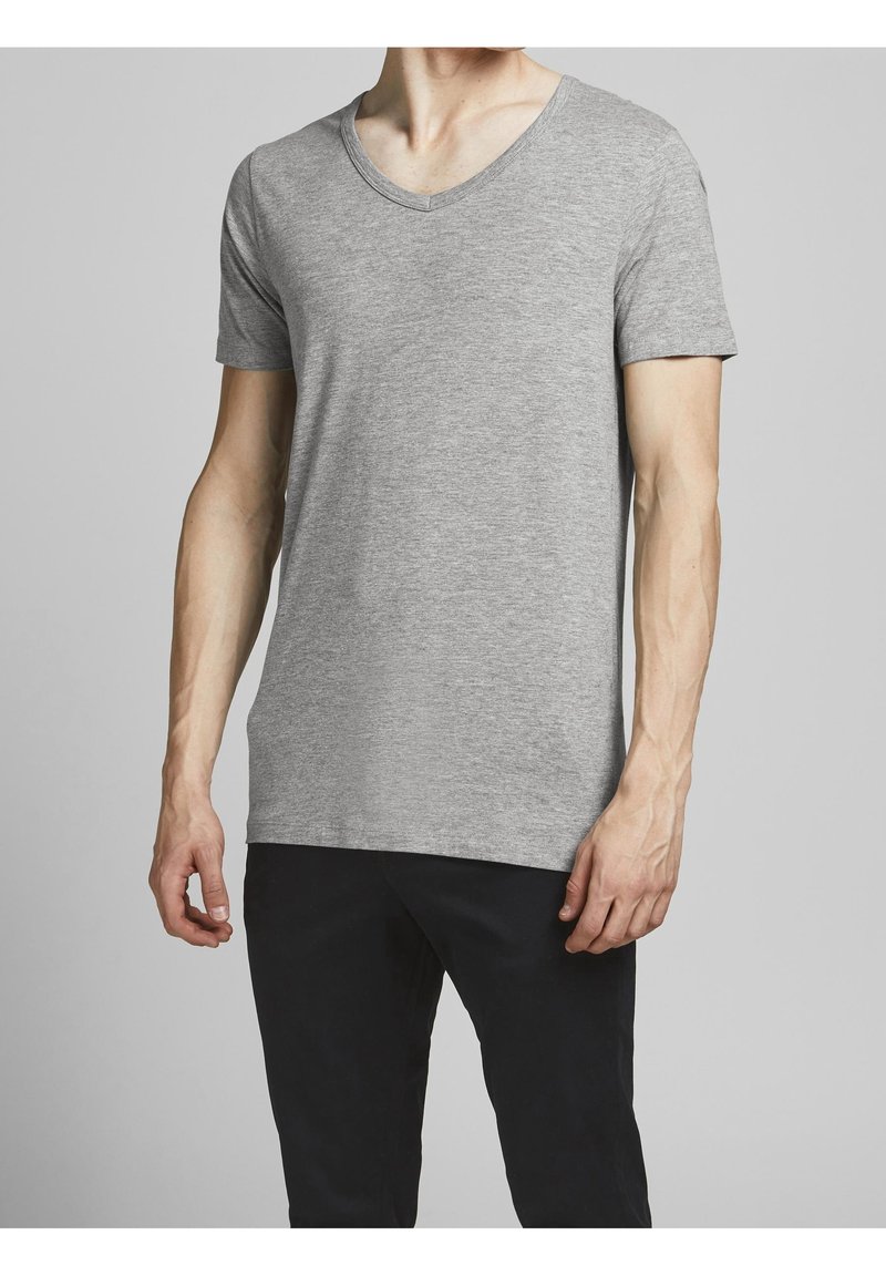 T-shirt gris à manches courtes avec col en V, fabriqué en tissu doux, présentant une coupe ajustée et une texture lisse, porté avec un pantalon foncé.