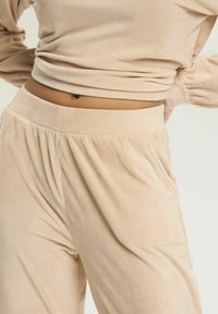 Beżowy, prążkowany zestaw loungewear składający się z dopasowanej bluzki i luźnych spodni z elastyczną talią oraz bocznymi kieszeniami.
