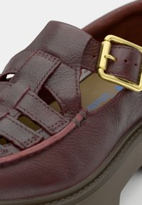 Bordeaux leren schoen met een uitgesneden ontwerp, ronde neus, verstelbare gouden gesp en een dikke, gestructureerde plateauzool.
