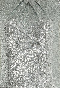 Tissu en sequins argentés avec une texture lisse. Présente un décolleté drapé et un effet dégradé allant de sequins denses à rares.