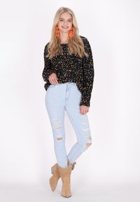 Fekete, textúrált pulóver, színes pöttyökkel, világoskék, szakadt skinny farmernadrággal és bézs bokacsizmával párosítva.