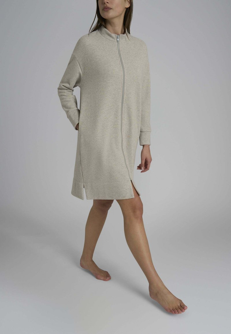 Abito zip-up grigio chiaro con maniche lunghe, spacco laterale e colletto alto, realizzato in un tessuto morbido con una texture liscia.