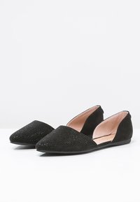 Zapatos planos negros con punta afilada, que cuentan con un upper texturizado y un acabado de ante suave. Los laterales están cortados para un perfil elegante.