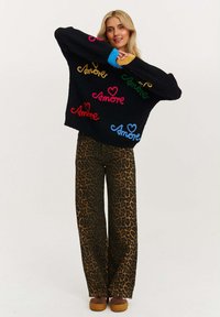 Czarny sweter dzianinowy z kolorowymi wzorami tekstu "Amore", w połączeniu z brązowymi spodniami w leoparda o szerokich nogawkach oraz brązowymi butami na platformie.