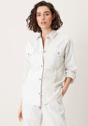 Camisa de mezclilla clara con botones en la parte delantera, dos bolsillos en el pecho y mangas enrolladas. Presenta una mezcla de texturas y un ajuste holgado.