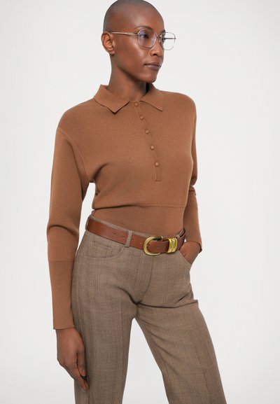 Pulover polo tricotat maro, cu guler și închidere cu nasturi, asortat cu pantaloni bej cu carouri și o curea maro cu cataramă aurie.