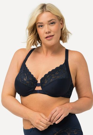 Navyblauwe beha met kantafwerking, gevormde cups en een diepe halslijn. Voorzien van verstelbare bandjes en een haak-en-oogsluiting aan de voorkant.