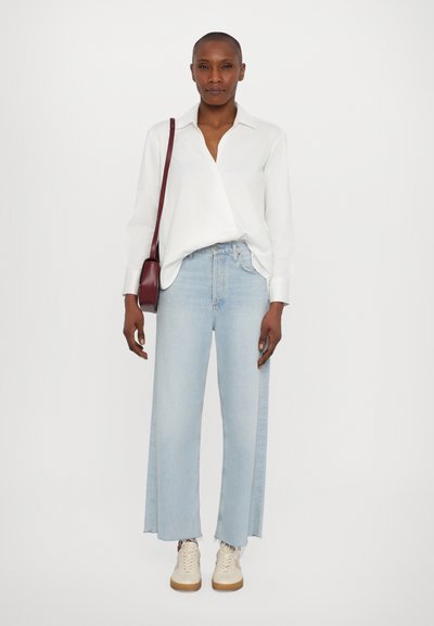 Ljusblå vida jeans med fransar i nederkant, parat med en vit, kragskjorta med långa ärmar. Tillbehören inkluderar en liten bordeauxfärgad crossbody-väska.