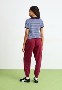 Navy polkadot kortærmet skjorte parret med bordeaux joggers. Outfittet har blødt stof, en afslappet pasform og elastiske manchetter. Sorte sneakers.
