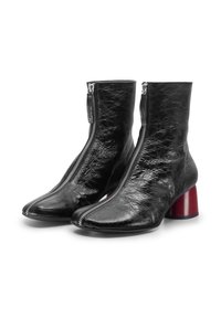 Stivaletti neri in pelle con punta a mandorla, cerniere metalliche e tacco a blocco rosso spesso. La texture ha una finitura rugosa.