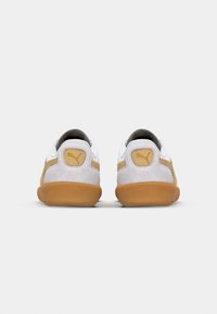 Pair of white and tan Puma sneakers shown from the back with gum soles on a white background.