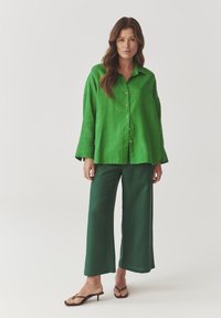 Green linen button-up shirt with long sleeves, paired with matching wide-leg trousers. Footwear features thin straps and a small heel.