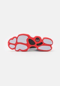 Semelle de chaussure avec bords rouges et sections antidérapantes blanches texturées, arborant un logo circulaire noir près du talon.