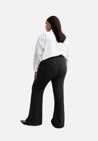 Camisa blanca de gran tamaño con mangas abullonadas, combinada con pantalones negros acampanados. La tela parece suave y ligera, adecuada para un look casual.