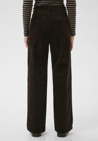 Pantalons en velours côtelé à jambes larges de couleur marron foncé, comportant des côtes verticales, des passants de ceinture et deux poches arrière. Texture lisse et coupe ajustée.