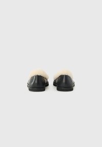 Pantofole nere in pelle con rivestimento in ecopelliccia crema e suola in gomma piatta, dotate di punta arrotondata e design minimalista.