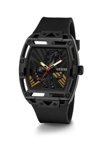 Montre-bracelet noire Guess avec un motif de cheval noir en relief sur le cadran, aiguilles dorées et rouges, et rayures diagonales dorées en arrière-plan.