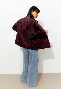 Veste matelassée bordeaux avec une coupe large et raccourcie et des poignets côtelés. Assortie à un jean à jambes larges bleu clair, présentée sur un fond blanc.