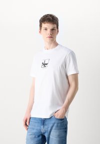 Camiseta blanca de algodón con mangas cortas y escote redondo, que presenta un diseño gráfico negro en un cuadro en el centro.