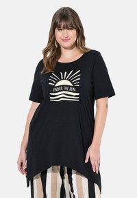Top negro de manga corta con dobladillo curvado, que presenta un gráfico del sol y el texto "BAJO EL SOL" en color crema. Material suave y de corte holgado.