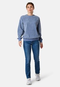 Felpa in corduroy blu chiaro con texture a coste, scollatura rotonda e maniche lunghe, abbinata a jeans blu e sneakers bianche.