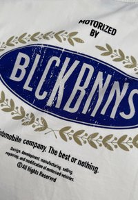 Witte stof met een blauw ovale logo met de tekst "BLCKBNNS" en gouden bladerenaccenten, met een versleten textuur. Aanvullende tekst eronder.