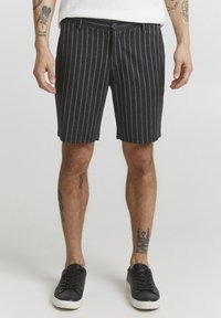 Shorts a righe grigio scuro con taglio dritto, chiusura con bottone, tasche laterali e orlo pulito. Indossati con sneaker nere.