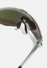 Sonnenbrille mit transparentem Rahmen, gebogenen dunklen Gläsern, verstellbaren Nasenpads und gravierten Logodetails an den Bügeln.
