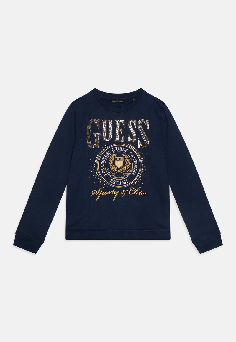 Námořnicky modrá mikina s dlouhým rukávem, která má velké logo "GUESS" z rhinestone, kulatý emblém a zlatý text "Sporty & Chic." Materiál je směs bavlny.