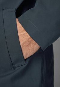 Jachetă impermeabilă de culoare albastru închis, cu o vedere detaliată a mânecii și buzunarului, având un material neted și cusături curate.