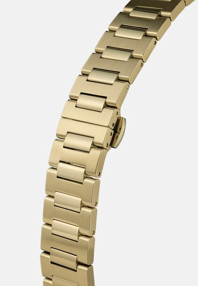Gouden metalen horloge-armband met brede, rechthoekige schakels en een verborgen sluiting, weergegeven tegen een effen lichte achtergrond.