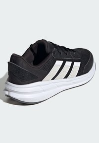 Czarne buty sportowe z siateczkową cholewką, białym wzorem w trzy paski, wyściełanym kołnierzem oraz miękką białą podeszwą dla komfortu i wsparcia.