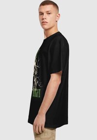 Sort bomulds T-shirt med et stort grafisk print af et træ og teksten "NIGHT" i levende grøn. Løs pasform med korte ærmer.