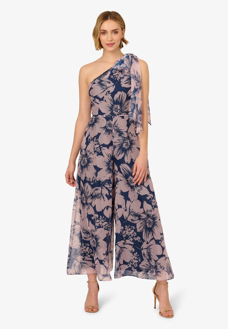 Bloemen jumpsuit met een een-schouder ontwerp, marineblauwe basis met lichtroze bloemen, vloeiende stof en een knoopaccent op de schouder.