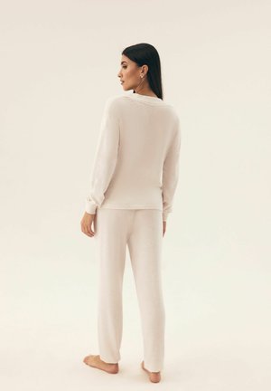 Beige Loungewear-Set bestehend aus einem Langarm-Oberteil und einer locker fallenden Hose. Weicher, strukturierter Stoff mit gerippten Bündchen und Saumakzenten.