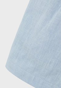 Helles blaues Leinengewebe mit einer subtilen Textur, das einen gesäumten Rand und Nähedetails zeigt. Das Material wirkt leicht und atmungsaktiv.