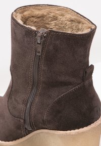Brown suede ankle boot with a zip closure, soft fur lining, rounded toe, and a light-colored platform sole. Stitch detailing accentuates design.
