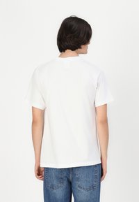Hvid bomulds t-shirt med rund halsudskæring og korte ærmer, med et minimalistisk design og et lille mærke på bagsiden.