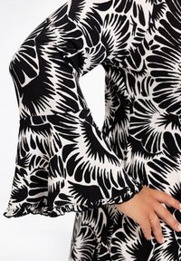 Schwarz-weißes Blümchenmuster-Kleid mit weit ausgestellt Ärmeln; weicher Stoff, geraffte Manschetten und mutiges grafisches Design.