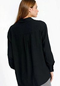 Czarna koszula z długim rękawem, z klasycznym kołnierzykiem, plisowanym tyłem i gładką teksturą. Tkanina miękko się układa.