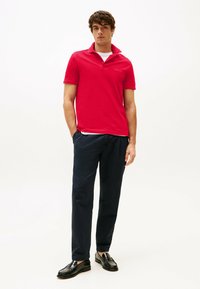 Rode polo shirt met een kraag, korte mouwen. Gecombineerd met donkerblauwe broek en zwarte instappers. Schone, vlakke texturen.